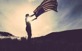 Man waving American flag in a field in front of mountain