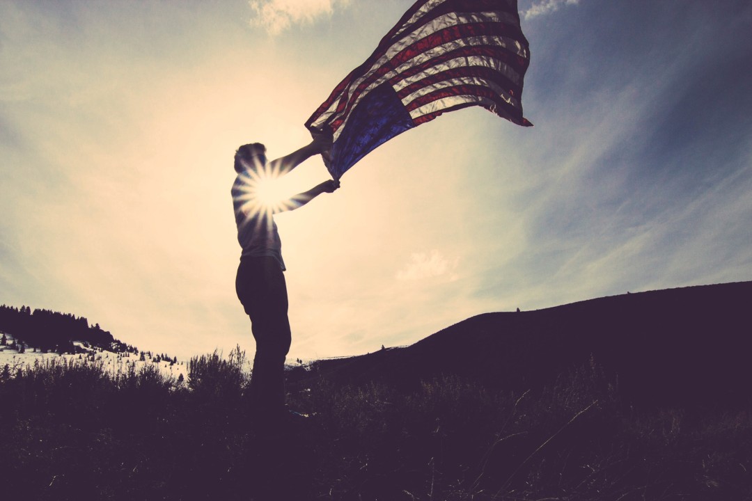 Man waving American flag in a field in front of mountain