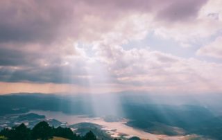 Rays of sunshine coming through the dark clouds above a river and mountain