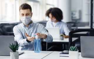 Employee using hand sanitizer and mask at desk job