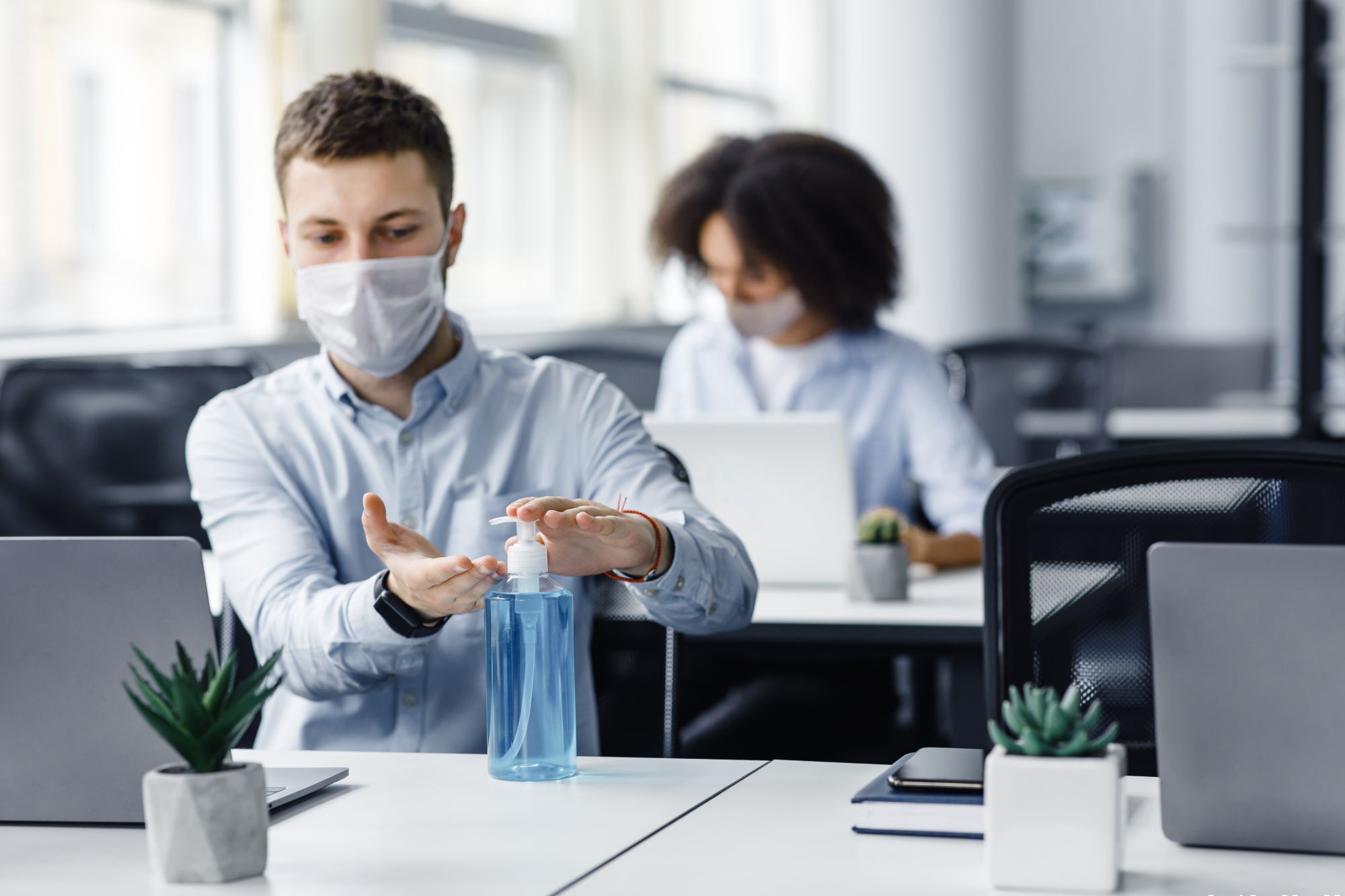 Employee using hand sanitizer and mask at desk job